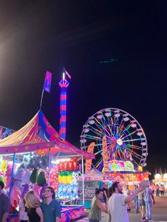 people are standing around in front of carnival rides and ferris wheel at the fairground