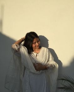 a woman standing in front of a white wall with her hands on her head and arms behind her head