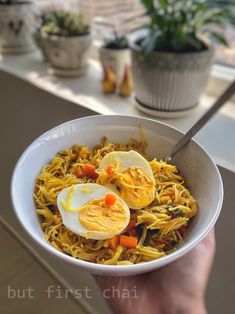 a person holding a bowl of noodles with hard boiled eggs