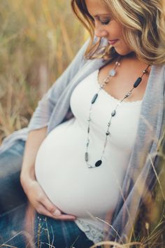 a pregnant woman sitting in the grass with her belly tucked up to her chest and wearing a necklace