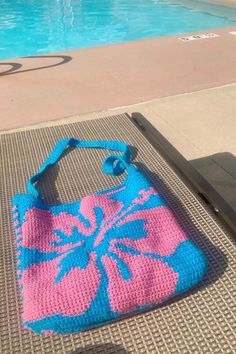 a pink and blue bag sitting on top of a mat next to a swimming pool