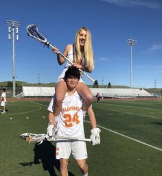 a woman is carrying a man on her shoulders while they both are wearing lacrosse uniforms