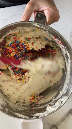 someone is decorating a cake with white frosting and sprinkles