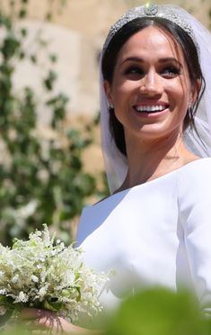 a woman in a white dress holding a bouquet and smiling at the camera while wearing a tiara