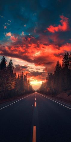 the sun is setting on an empty road with trees in the foreground and clouds in the background