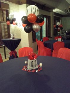 a room filled with tables and chairs covered in black tablecloths, red chair covers and balloons