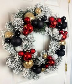 a christmas wreath with red, black and gold ornaments hanging on the front door to welcome guests