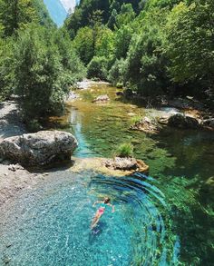 a person swimming in a river surrounded by trees and rocks with clear blue water below