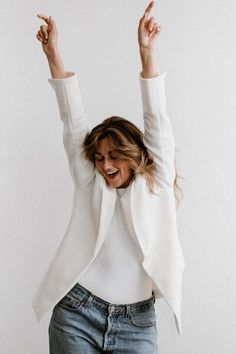 a woman with her arms in the air and hands up, wearing jeans and a white jacket