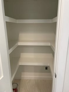 an empty closet with white shelving in it and a can of paint on the floor