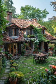 an outdoor patio with tables and chairs in front of a house surrounded by greenery