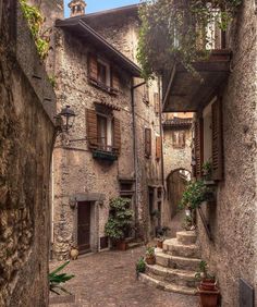 an alley way with stone buildings and steps leading up to the second floor, surrounded by greenery