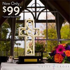 a white cross sitting on top of a table next to a vase filled with flowers