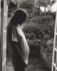 black and white photograph of a pregnant woman looking out an open door at a garden