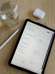 an electronic device sitting on top of a wooden table next to a glass and pen