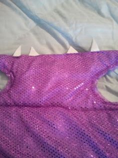 a purple sequin dress laying on top of a white sheet covered in plastic shark teeth