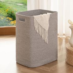 a grey basket sitting on top of a wooden floor next to a vase and window