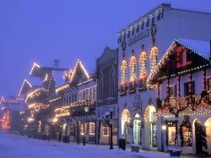 a row of buildings covered in christmas lights on a snow covered street during the day