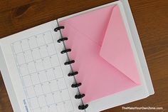 an open pink paper on top of a spiral - bound notebook with a calendar in the middle