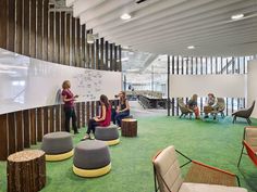 several people are sitting around in an office with green carpet and whiteboards on the wall