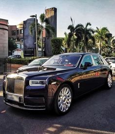 a black rolls royce parked in front of a building with palm trees on the other side