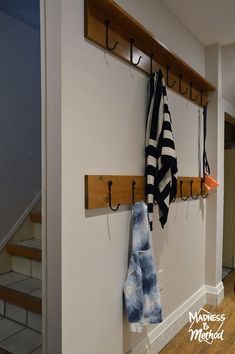 the coat rack has two coats hanging from it's hooks and is next to a stair case