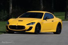 a yellow sports car driving down a road next to some grass and trees in the background