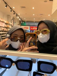 two women wearing face masks and holding up their cell phones in front of the camera