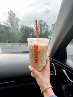 a person holding up a drink in their hand while driving down the road with trees in the background