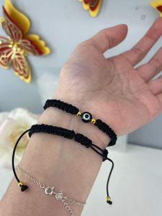 the hand is holding two bracelets with evil eye charms on it and black cord