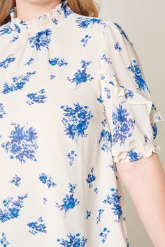 Deep dive in this tonal blue floral blouse that features a high ruffle neck and short puff sleeves. A relaxed fit is maintained throughout the bodice making it perfect for wearing it tucked into a pair of high rise bottoms. Pair it with medium washed denim or make it a set with the matching High Tide Eden Flared Mini Skirt.- Relaxed fit- High neck- Ruffle details- Keyhole- Color: Ivory BlueSize + Fit - Model is 5'10" and wearing size 2X- Measurements taken from size 2X - Chest: 51"- Length: 29" Flowy Smocked Top With Floral Print And Short Sleeves, Blue Top With Gathered Short Sleeves, Flowy Short Sleeve Blouse With Smocked Bodice, Blue Blouse With Gathered Short Sleeves, Blue Floral Print Ruffle Sleeve Blouse, Daywear Smocked Top With Short Gathered Sleeves, Daywear Smocked Top With Gathered Short Sleeves, Blue Smocked Bodice Top With Short Sleeves, Blue Floral Print Blouse With Ruffle Sleeves