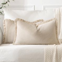 a white couch with three pillows on top of it next to a potted plant