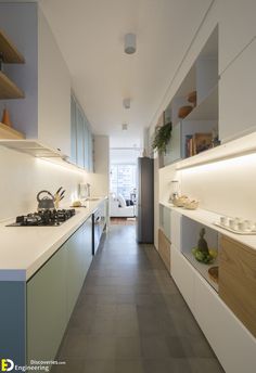 a long narrow kitchen with white counter tops and wooden shelves on either side of the room