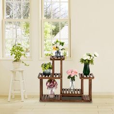 three wooden shelves with vases and flowers on them in front of two large windows