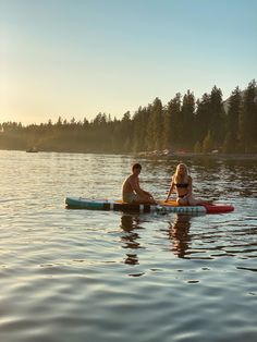 two people sitting on surfboards in the water with trees in the backgroud