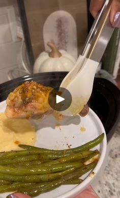 a person is holding a fork over some food on a plate with green beans and mashed potatoes