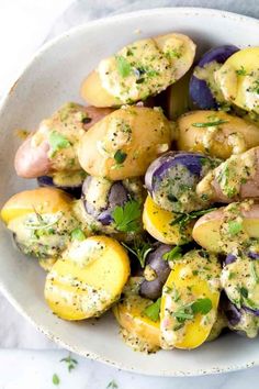 a white bowl filled with potatoes covered in herbs and seasoning sitting on a marble surface