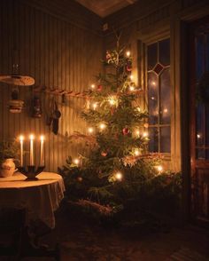 a lit christmas tree in the corner of a room next to a table with candles on it