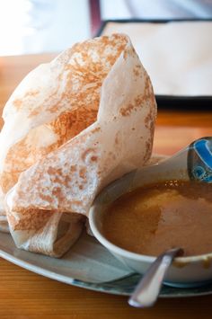 a bowl of soup and some pita bread on a plate with a spoon next to it