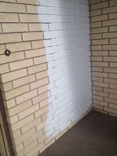 a white brick wall next to a metal grate on the floor in front of it