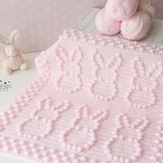 a pink crocheted blanket next to a teddy bear and some balls of yarn