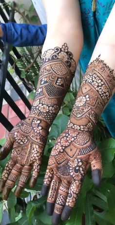 two hands with henna tattoos on them and green leaves in the foregrounds