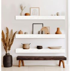 three white shelves with vases, bowls and other items on them in a room