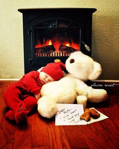 a baby sleeps next to a teddy bear in front of a fireplace with a note written on it