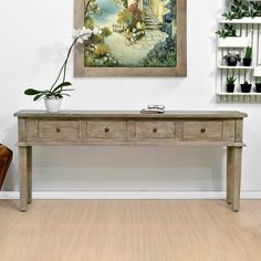 a painting hanging on the wall next to a table with two drawers and a potted plant