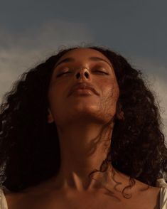 a woman with her eyes closed, looking up at the sky and clouds in the background