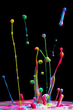 colorful paint splattered on top of a black surface with different colored sticks sticking out of it