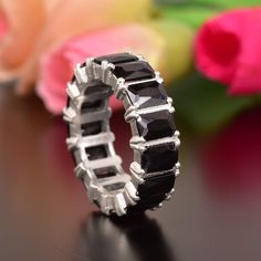 a black diamond ring sitting on top of a table next to pink flowers and tulips