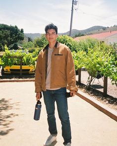 a young man holding a wine bottle in his right hand while standing on the sidewalk