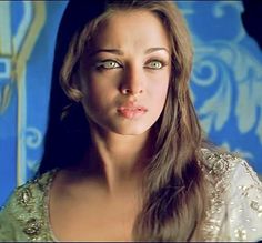 a woman with long brown hair and green eyes posing for a photo in front of a blue wall